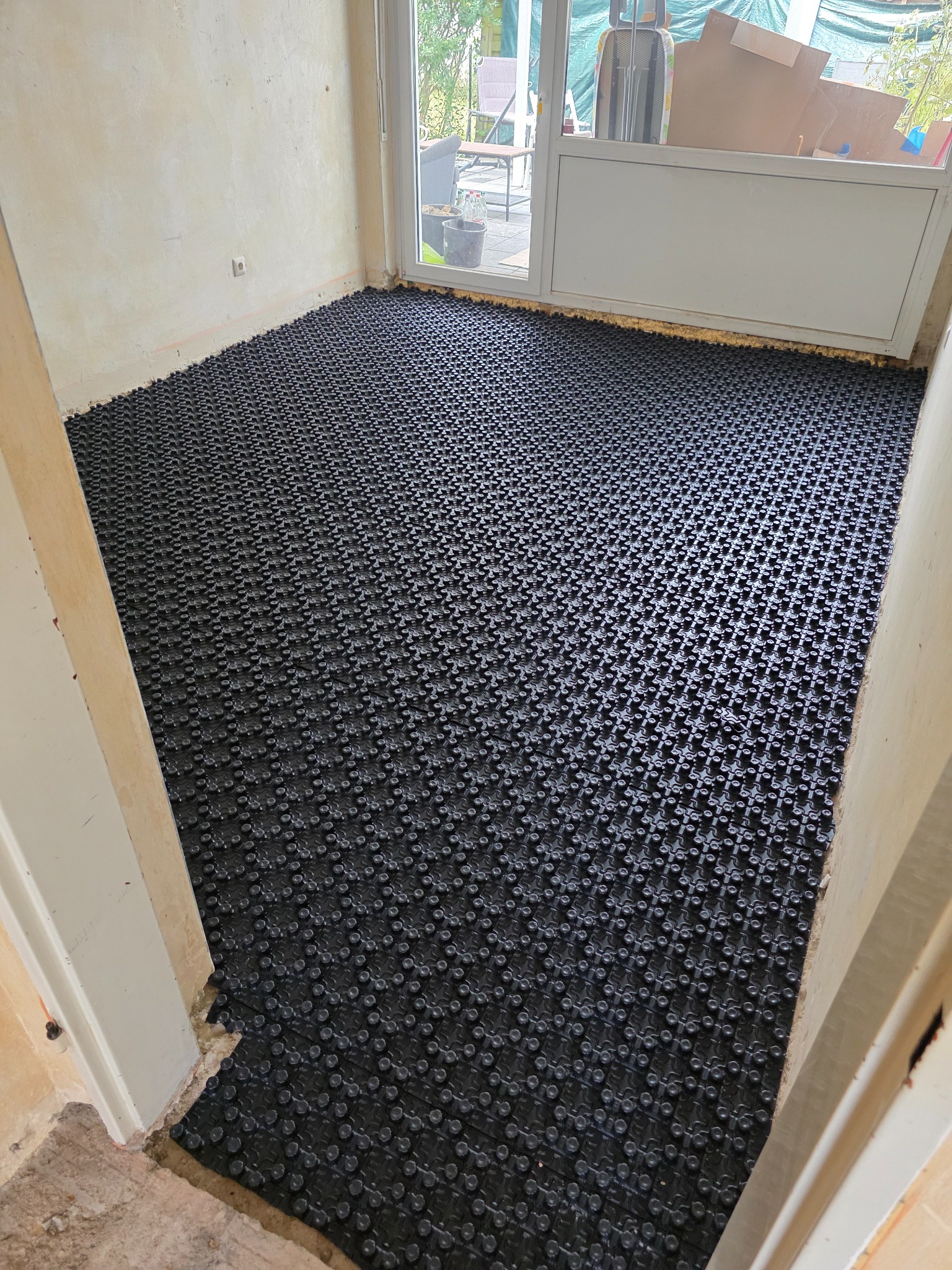 Schwarze Noppenplatten auf dem Boden eines Raumes vor der Heizrohrverlegung