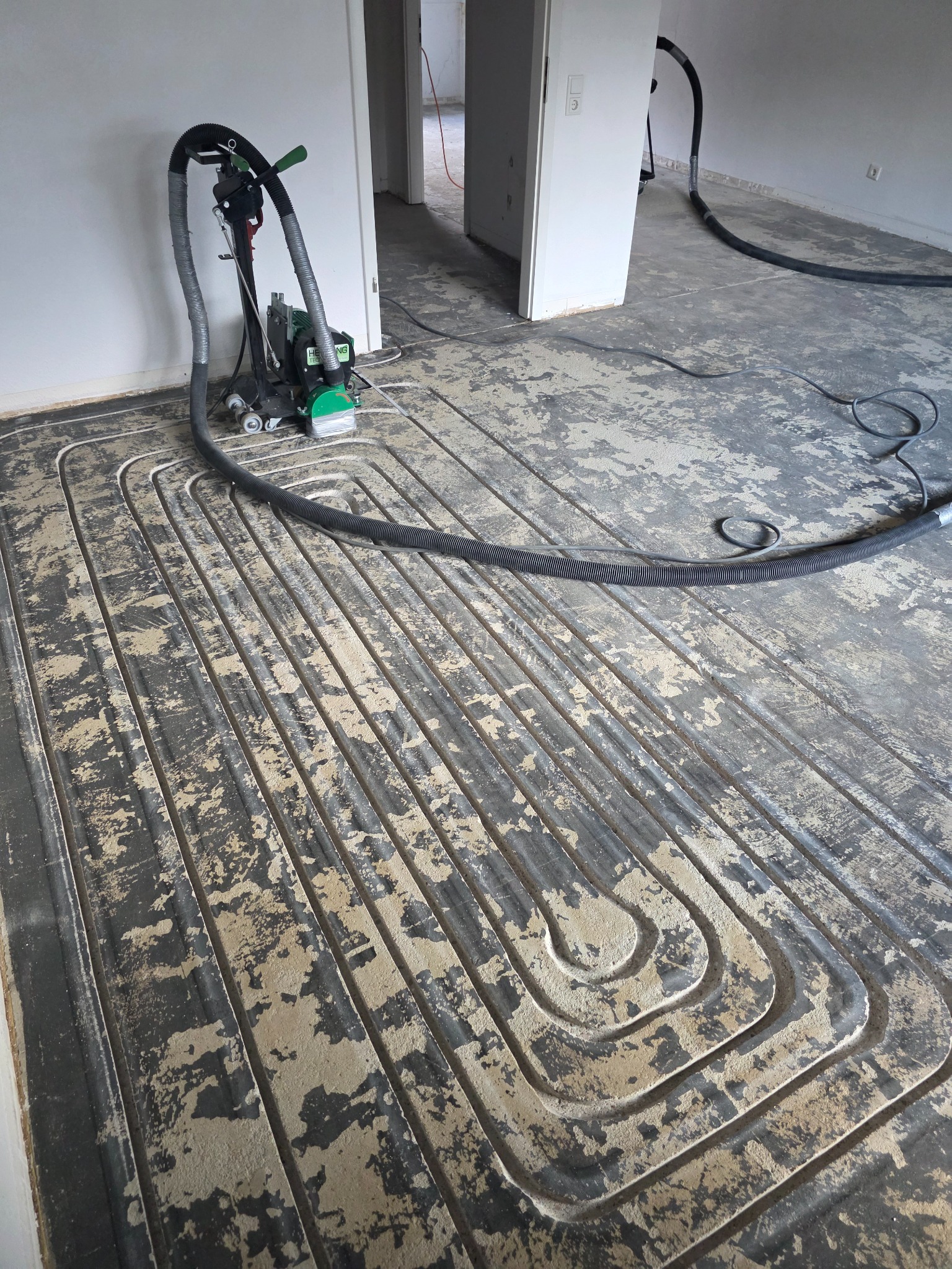 Fräsmaschine mit Absaugschlauch neben Heizkanälen im vorhandenen Estrich