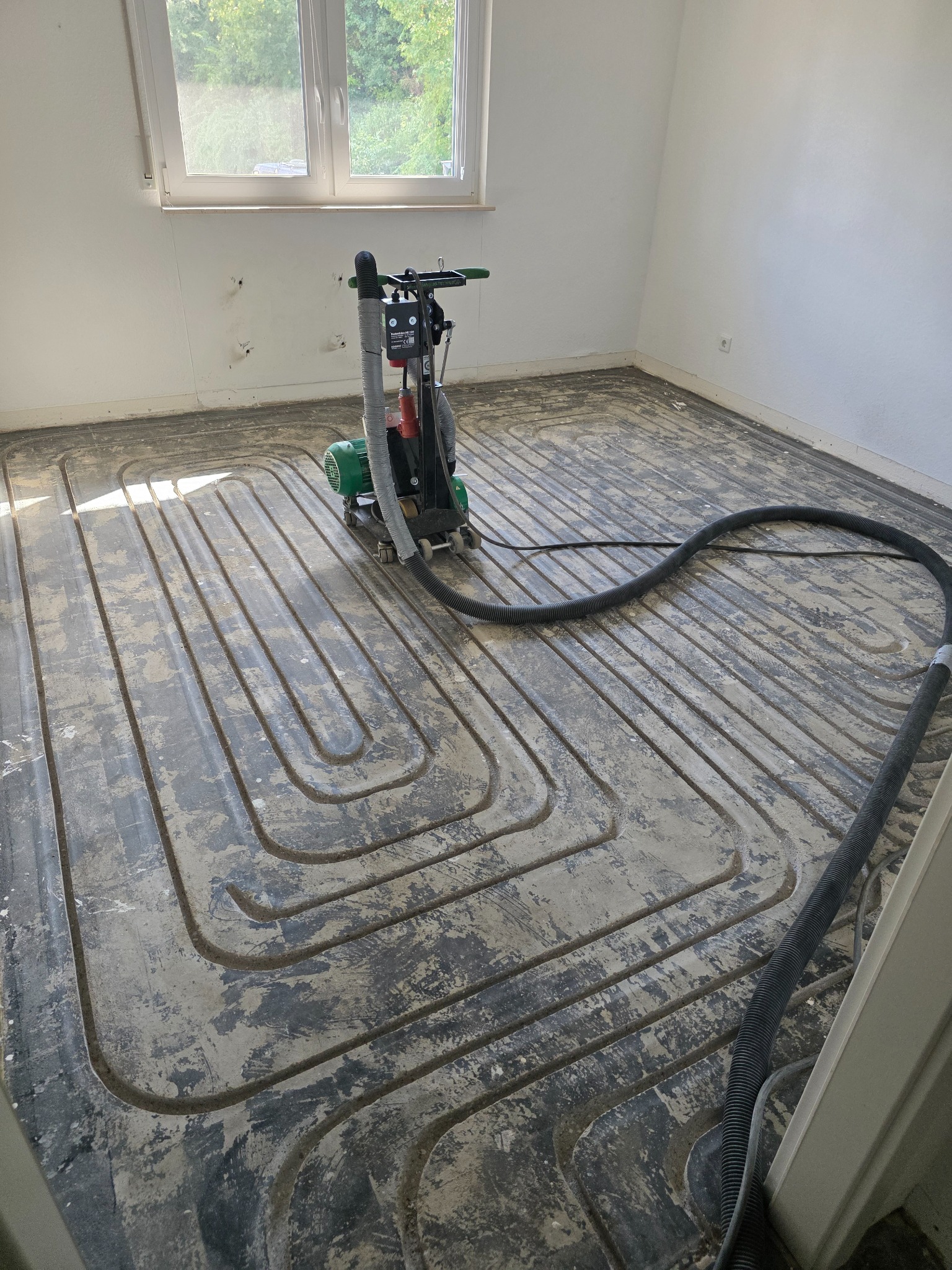Fräsmaschine mit angeschlossenem Absaugschlauch auf einem gefrästen Estrichboden