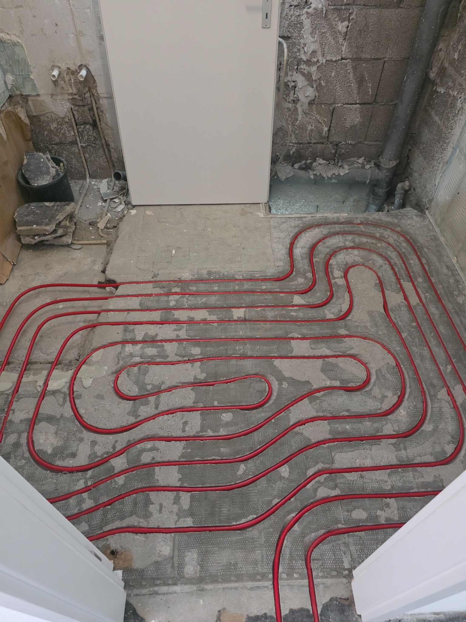 Verlegte rote Heizrohre im gefrästen Estrich eines Badezimmers mit Vorwandinstallation