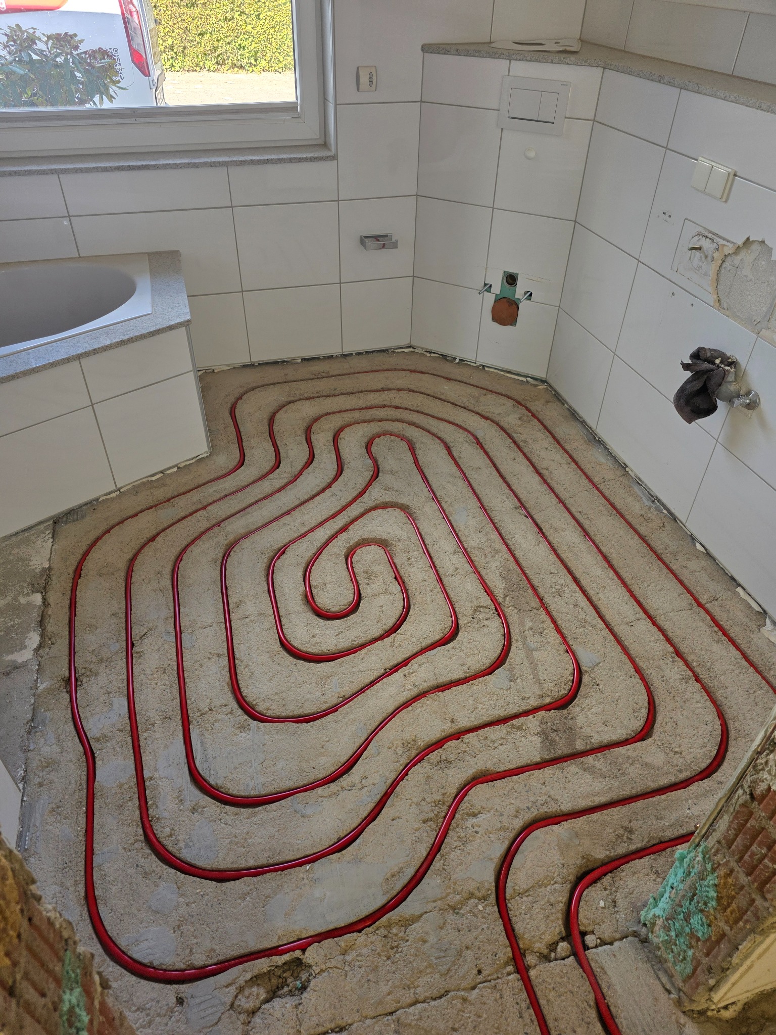Rote Heizrohre im gefrästen Estrich eines Badezimmers neben der Badewanne